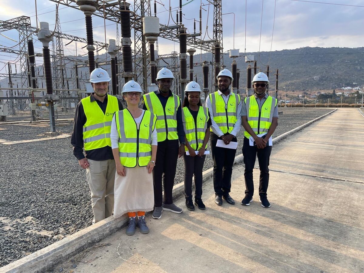 Six people in hard hats and high-visibility vests at a high voltage substation